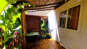 A wooden deck with a table and chairs, surrounded by lush greenery and a corrugated metal roof. - Moorea - Tropical Nest (Moorea-Maiao)