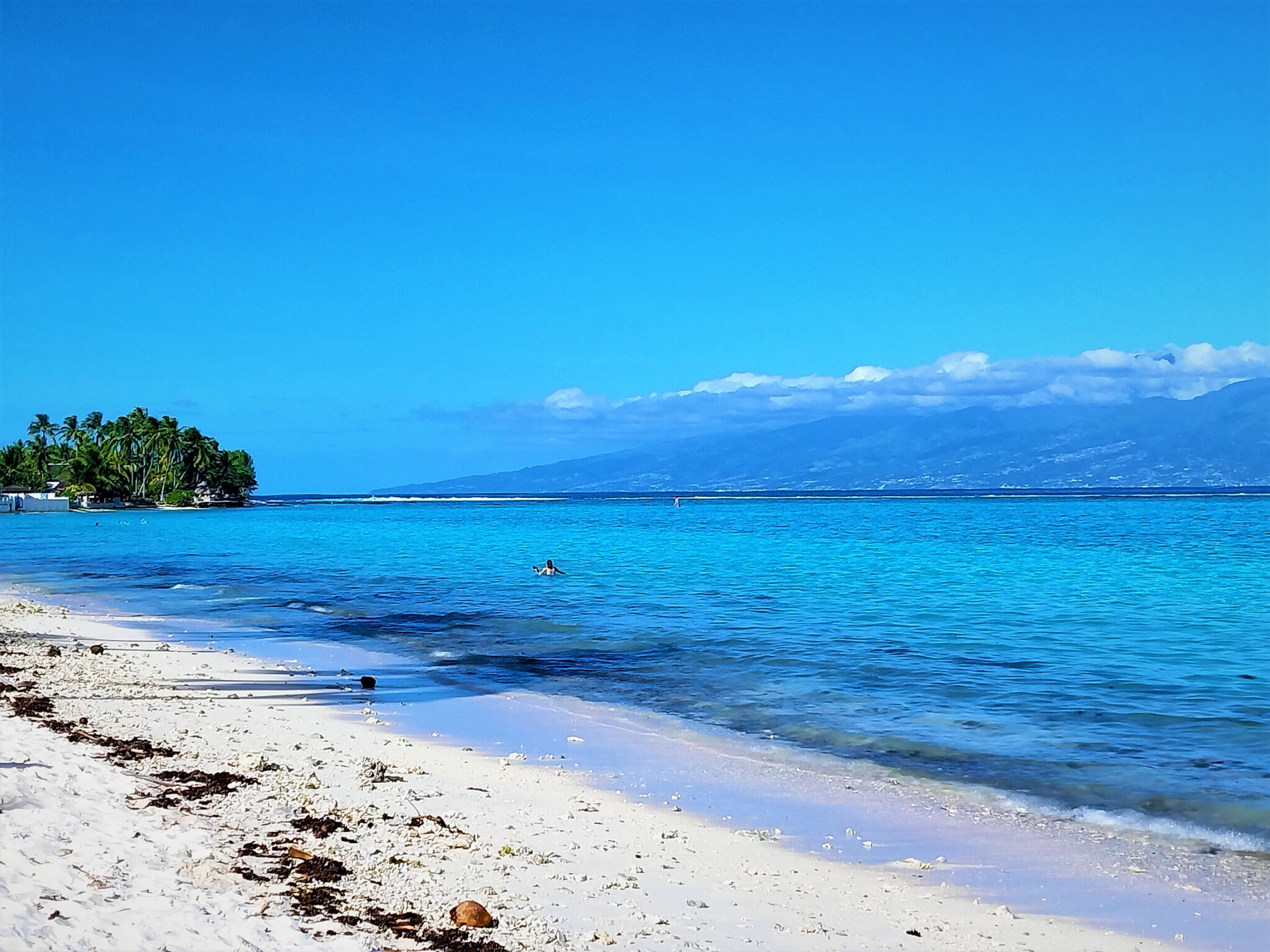 Una playa con aguas turquesas cristalinas, arena blanca y una pequeña isla con palmeras.