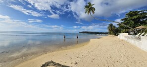 A beach with clear water, palm trees, and a white building with lounge chairs. - Moorea - Tropical Bungalow (Moorea-Maiao)