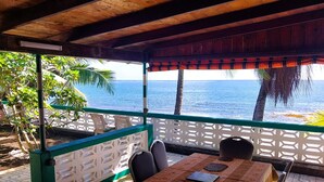 A covered outdoor seating area with a table and chairs, overlooking the sea. - Tahiti - Matavai Bay Cottage (Arue)