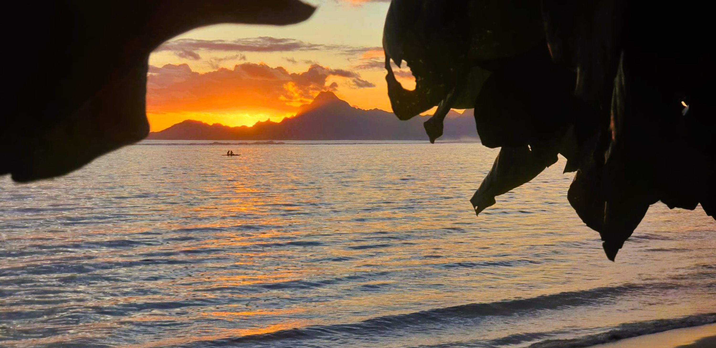 A sunset over a calm sea with a silhouette of mountains in the background.