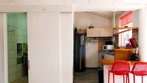 A compact kitchen with a refrigerator, microwave, and a small countertop. There are two red chairs and a window with a red blind. - Tahiti - Terevete Pool Studio (Arue)