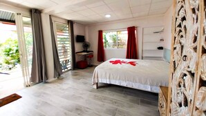 A hotel room with a bed, a desk, a chair, a TV, and a window with curtains. - Tahiti - Terevete Pool Studio (Arue)