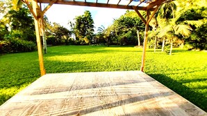 A wooden deck with a pergola overhead, surrounded by lush greenery and palm trees. - Tahiti - Haumaru Beach Fare (Mahina)