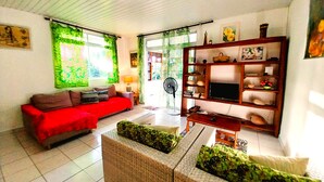 A living room with a red sofa, a wooden TV stand, and a fan. - Tahiti - Haumaru Beach Fare (Mahina)