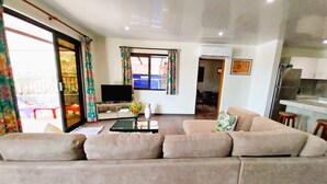 Een woonkamer met een bank, een salontafel, een televisie en een keuken in de achtergrond.