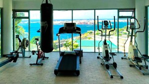 Ein Fitnessstudio mit einem Schlagbeutel, Laufbändern und Trainingsgeräten, mit Blick auf das Meer und die Stadtlandschaft.