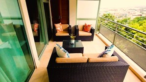 Ein Balkon mit Korbmöbeln, einem Deckenventilator und Blick auf die Stadt.