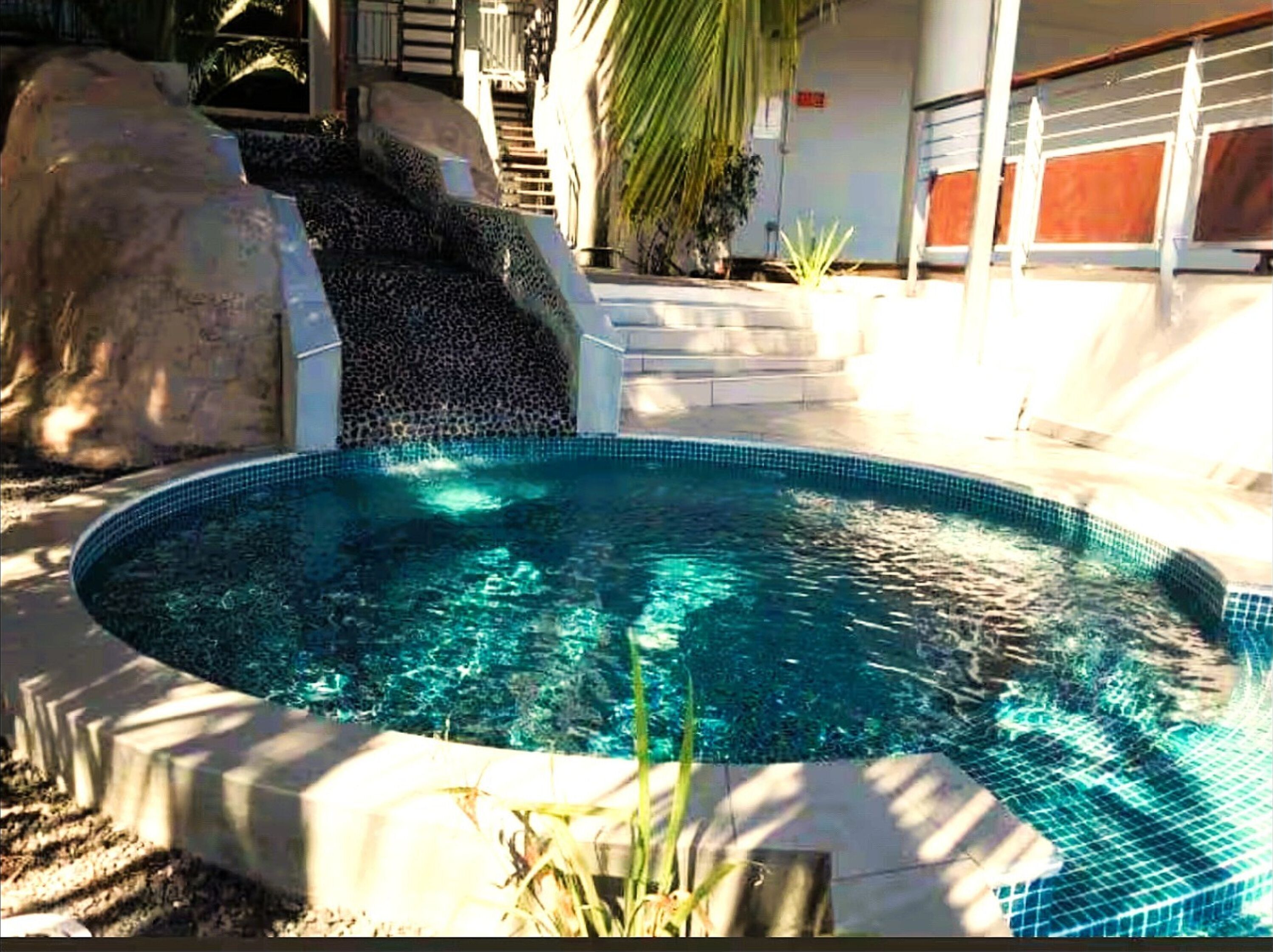 Una piscina circular con agua cristalina, rodeada por una solera de concreto y grandes rocas.