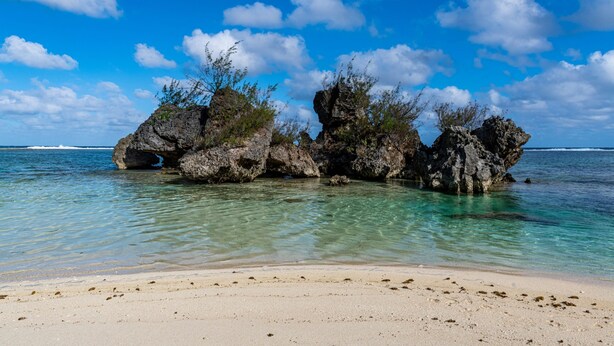 Une plage de sable fin, parsemée de formations rocheuses, où l’eau est calme.