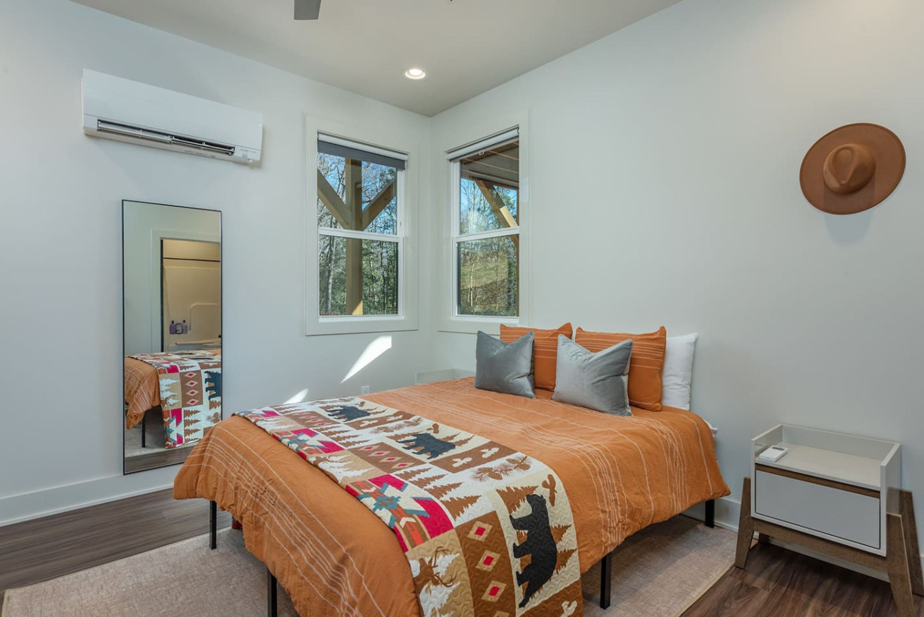 A bedroom with a large bed, a mirror, two windows, and a wall-mounted hat.