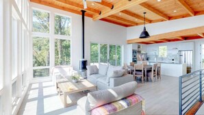 A spacious living area with a high ceiling, large windows, a sofa, a coffee table, and a dining area.