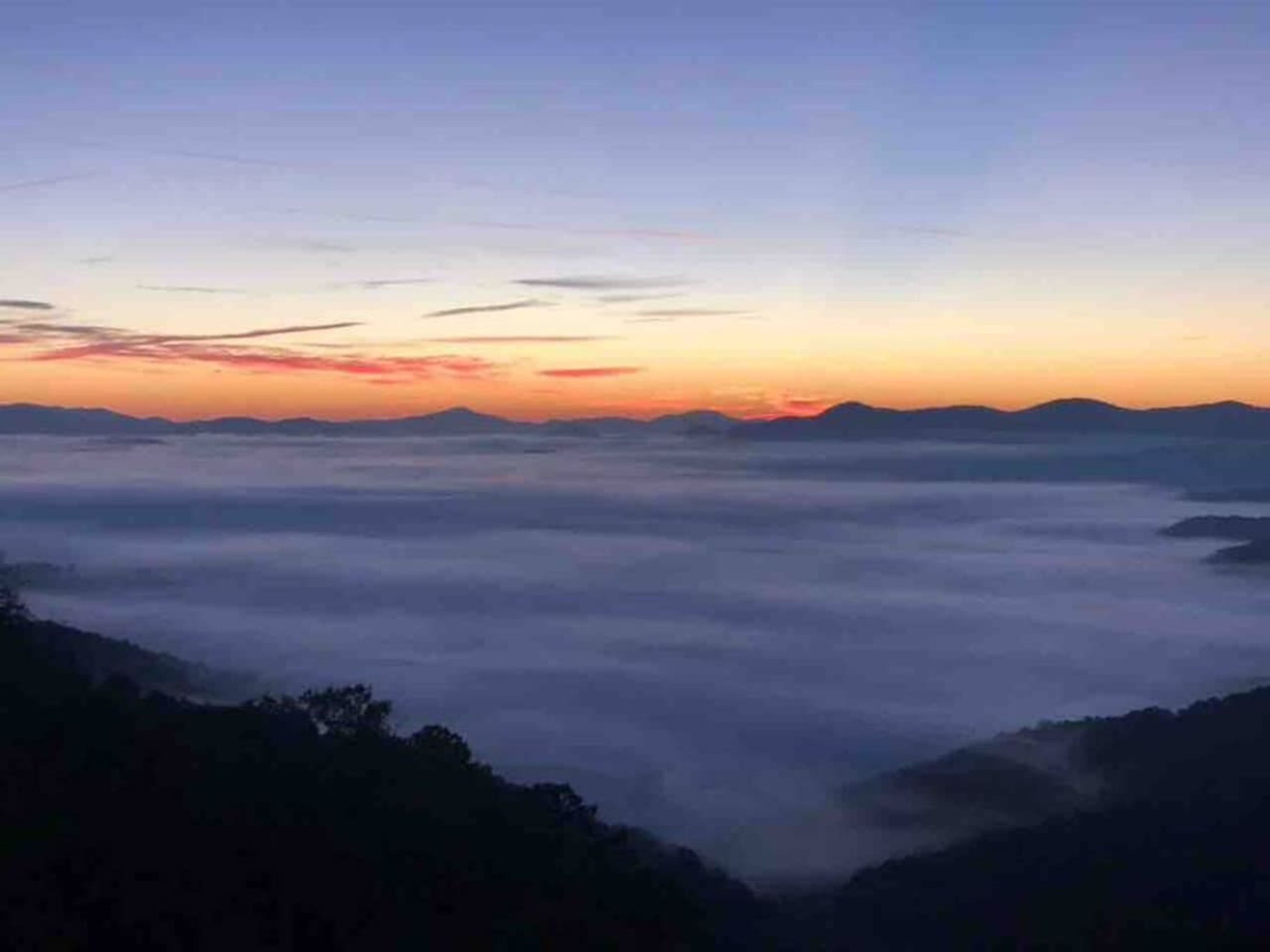 A mountainous landscape at sunrise with a view of the horizon and distant mountains.