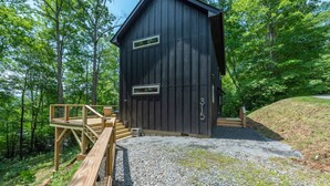 Una baita di legno con vialetto sterrato e veranda in legno, immersa nel verde alberato.