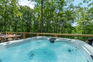 A hot tub surrounded by a wooden deck with a table and chairs, set in a forested area. - Hot Tub Nestled in the Forest w Chef s Kitchen (Canton)