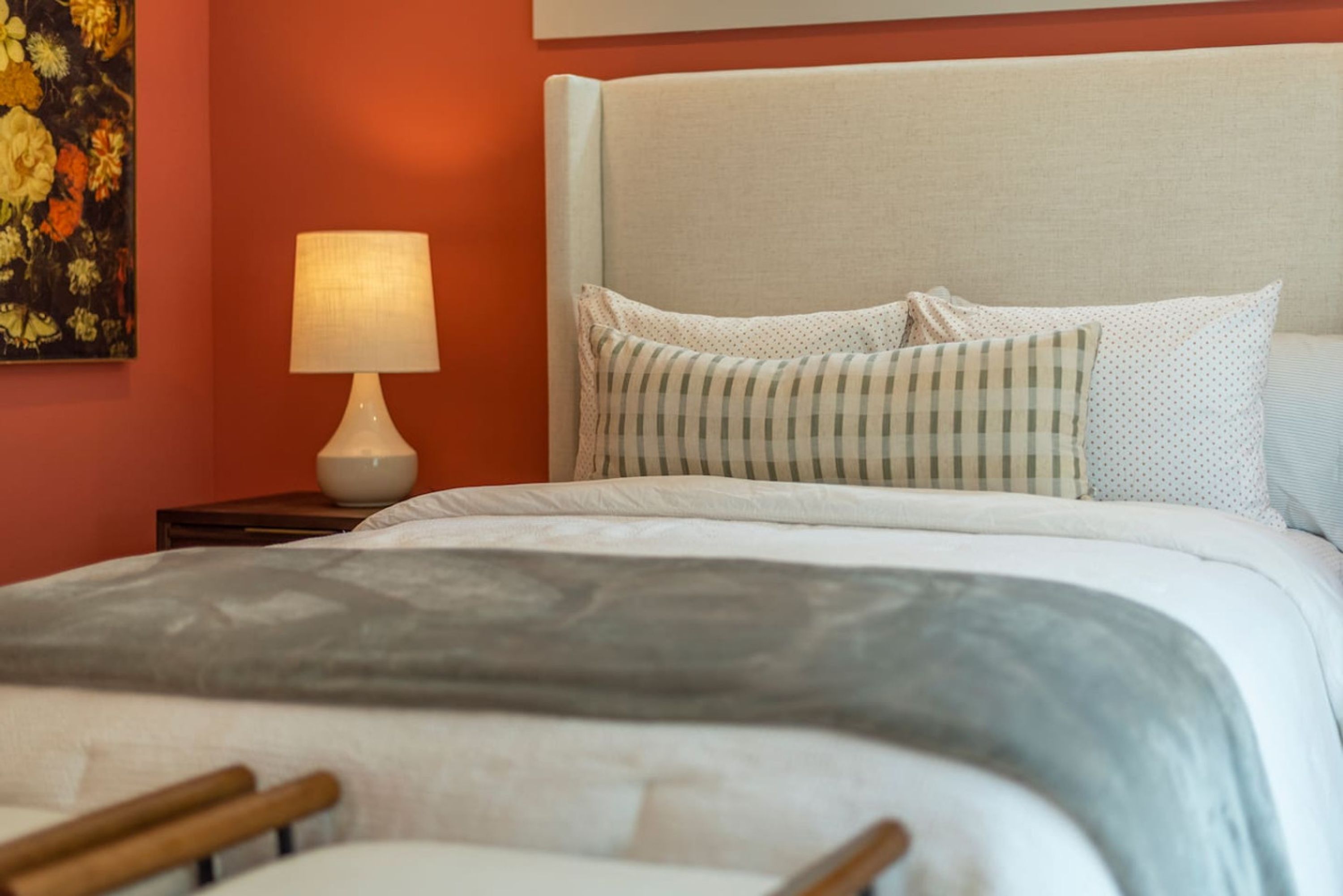 Una cama bien hecha con un cojín de cuadros y una lámpara en la mesita de noche.