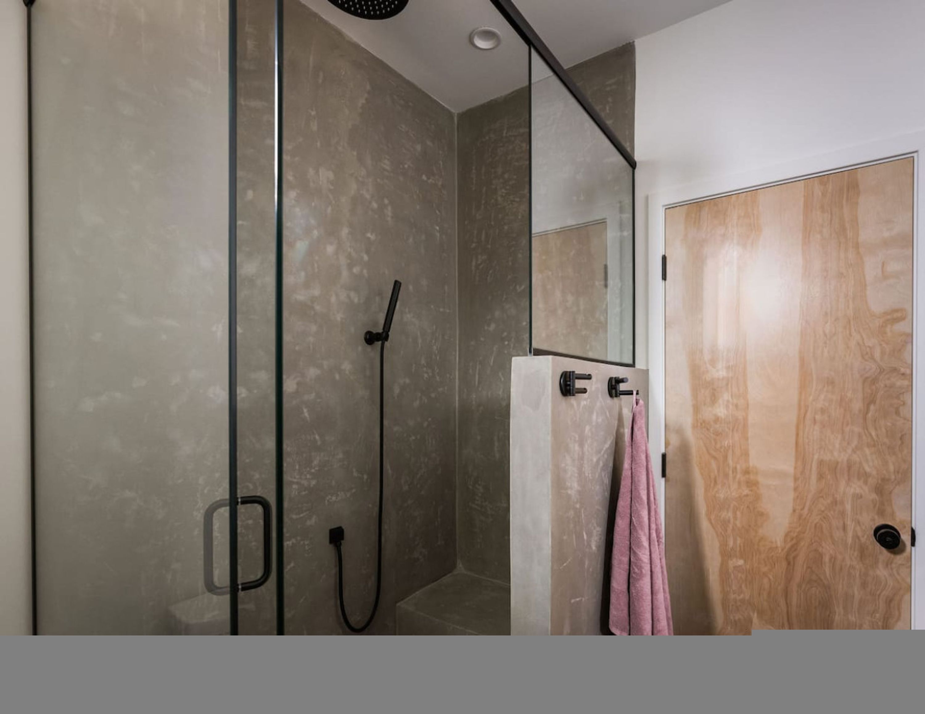 Un baño moderno con cabina de ducha de vidrio, una puerta de madera y un espejo.