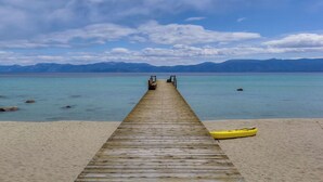 Un muelle de madera que lleva a una playa con un kayak sobre la arena.