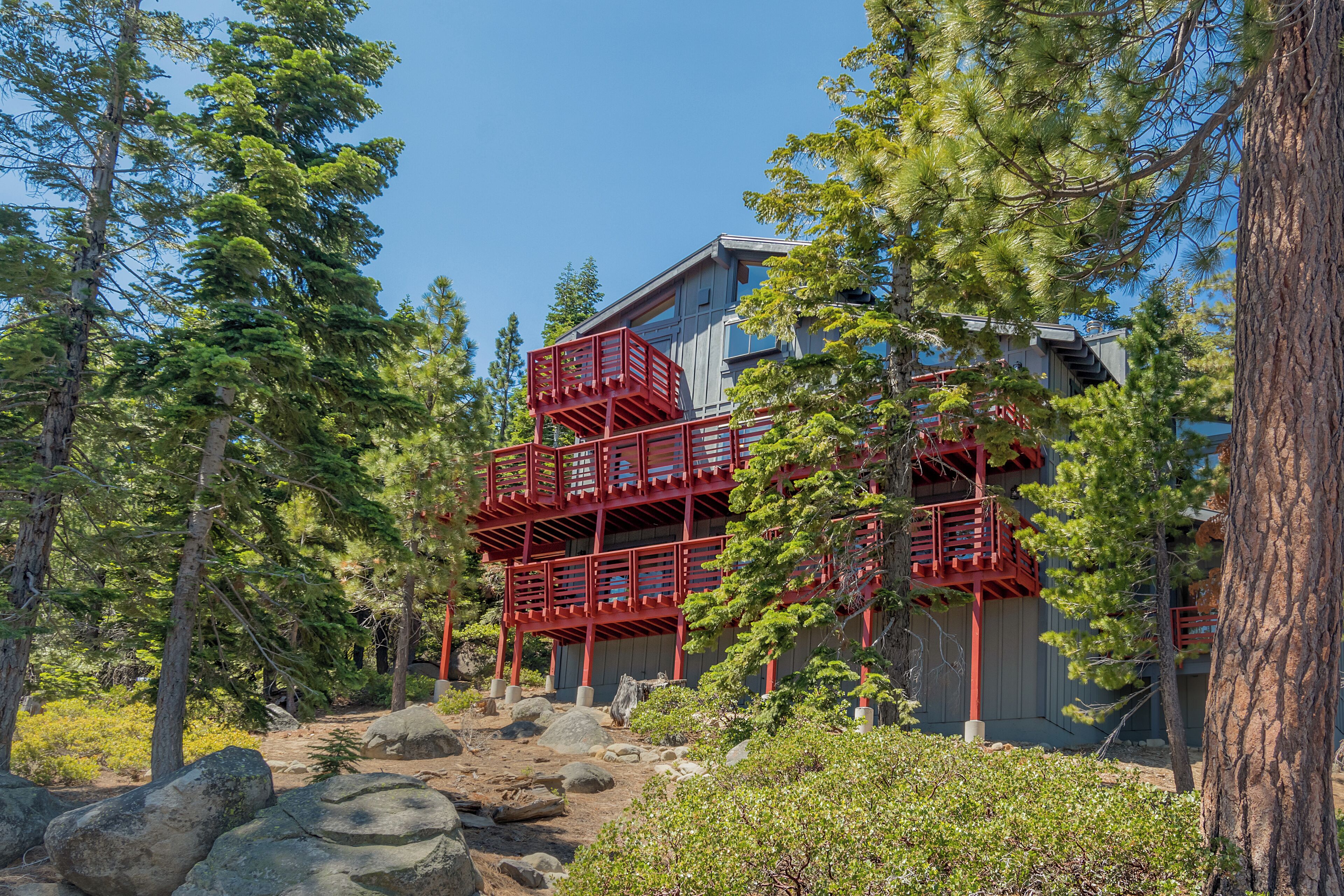 A multi-story building with a red exterior and a wooden deck, surrounded by trees and rocks.