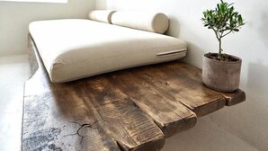 Habitación minimalista con una estantería de madera suspendida, un cojín y una planta en maceta.