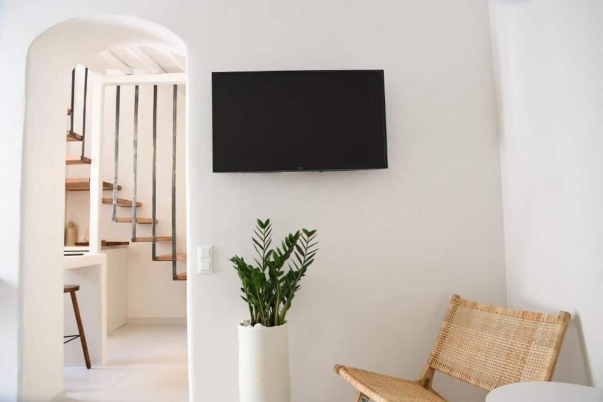 Um interior moderno com escada, televisão de tela plana na parede, planta em vaso e uma cadeira de vime.