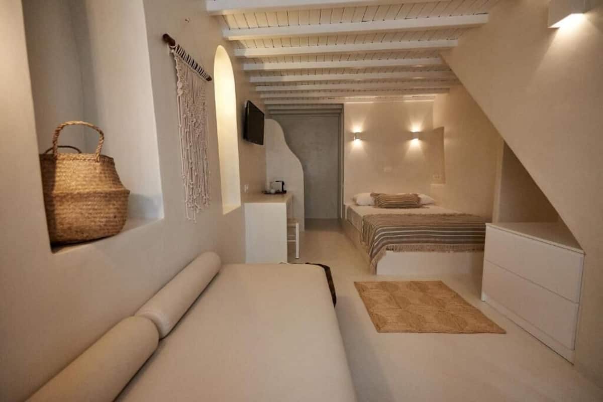 Quarto com cama, escrivaninha pequena, televisão na parede e um pendente de macramé.