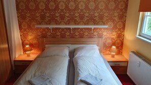A double bed with two nightstands, each with a lamp, in a room with patterned wallpaper and a window. - Vacation apartment in the manor house - directly opposite the castle with terrace and WLAN (Gablenz)