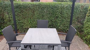 Een terras met een tafel en stoelen, omgeven door een haag.