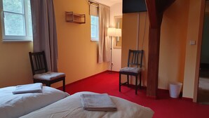 Een hotelkamer met twee bedden, een rood tapijt, twee stoelen, een lamp en een raam met gordijnen.