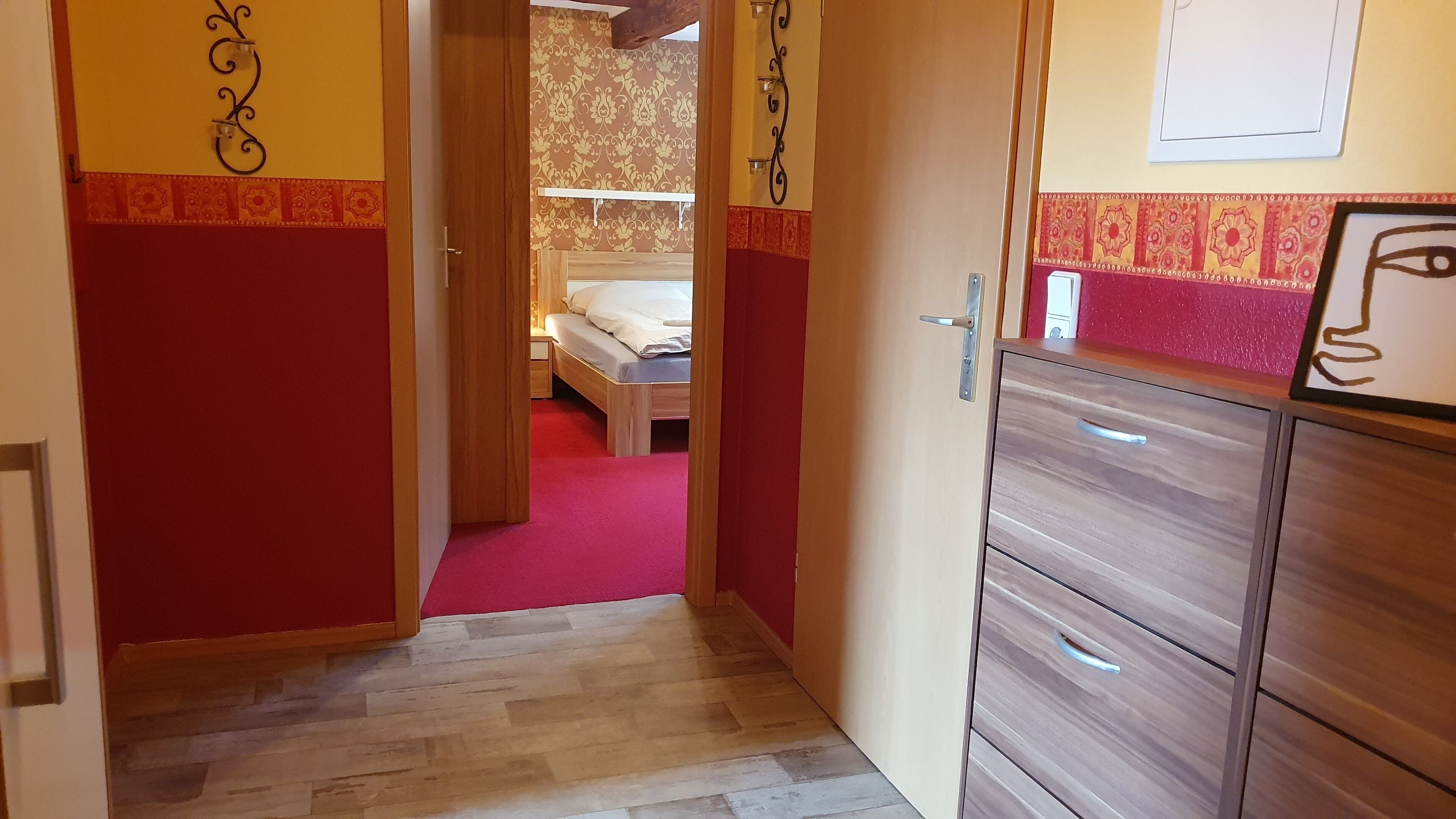 A hotel room with a wooden floor, a bed with white bedding, a red carpet, and a wooden wardrobe.