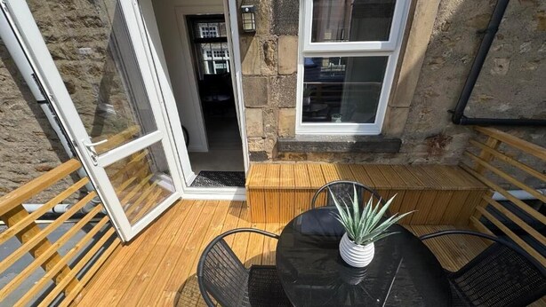 An open patio with a round table and chairs, a potted plant, and a wooden bench.
