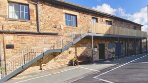 A stone building with a staircase leading to a balcony, a bench, and a sign indicating "CROWS HOTEL Rooms 1, 2, 3".
