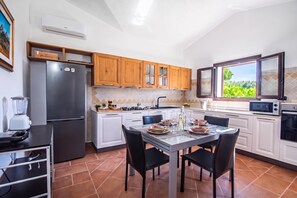 A modern kitchen with a dining area, featuring a refrigerator, stove, microwave, and a window with a view. - La Suara Manna (Telti)