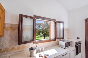 A kitchen with a window, a microwave, and a wine glass. - La Suara Manna (Telti)