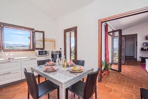 A modern kitchen with a dining area, large windows, and a view of the countryside. - La Suara Manna (Telti)