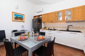 Een moderne keuken met witte kasten, een roestvrijstalen koelkast en een eethoek met een glazen tafel en zwarte stoelen.