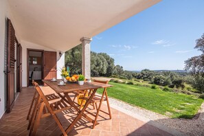 An outdoor patio with a wooden table and chairs, a potted plant, and a view of a green landscape. - La Suara Manna (Telti)