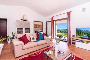 A living room with a sofa, a TV, a bookshelf, and a view of a mountain landscape. - La Suara Manna (Telti)