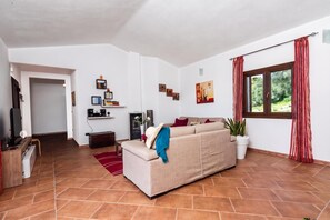 A living room with a sofa, a television, a bookshelf, and a window with curtains. - La Suara Manna (Telti)