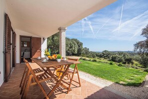 An outdoor patio with a wooden table and chairs, a potted plant, and a view of a green landscape. - La Suara Manna (Palau)