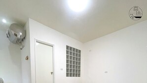Une chambre à coucher au style minimaliste, avec un lit, une petite table de chevet, une fenêtre à carreaux et un tapis rond à motifs.