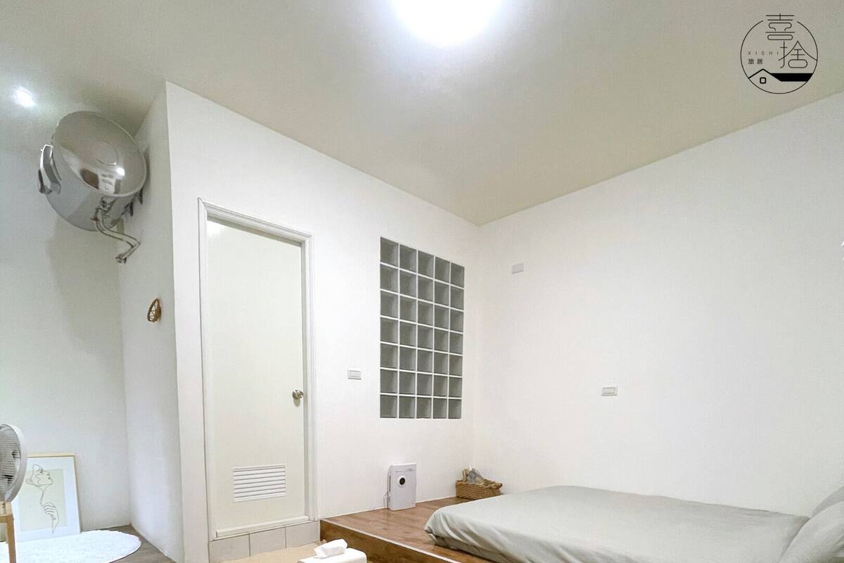A minimalist bedroom with a bed, a small bedside table, a window with a grid pattern, and a round patterned rug.