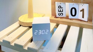 Une table de chevet en bois avec une horloge numérique affichant 23 h 02, une lampe et un calendrier marqué du 1er septembre.