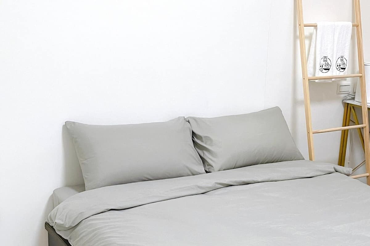 A bed with grey bedding and a wooden ladder against a white wall.