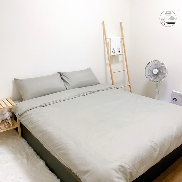 A bed with a grey mattress and pillows, a wooden ladder leaning against the wall, and a standing fan on the floor. - Xishi Stay (Tainan)