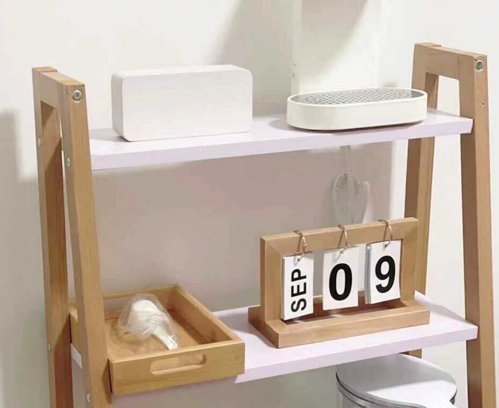 A wooden shelf unit with a white electronic device on the top shelf and a wooden tray with a plastic bag on the bottom shelf.