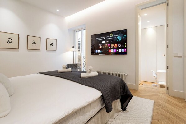 A modern bedroom with a large bed, a flat-screen TV mounted on the wall, and framed artwork above the bed. - NEW area. Premium Apartment in Retiro area (Madrid)