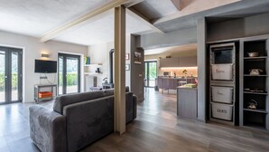 A modern living room with a grey sectional sofa, a flat-screen TV, and a kitchen area with labeled storage bins for plastic, paper, and glass. - Wonderful private villa for 6 people with private pool, WIFI, TV, patio and pets allowed (Bossolasco)