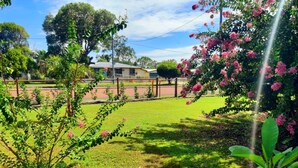 A grassy area with a fence, trees, and a building in the background. - Oakwood House at Wild Wood Park Retreat | 5-Bedroom home for Families & Groups (Tambo)