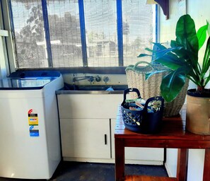 Eine kompakte Küche mit Spüle, kleinem Kühlschrank und einem Fenster mit Jalousien.